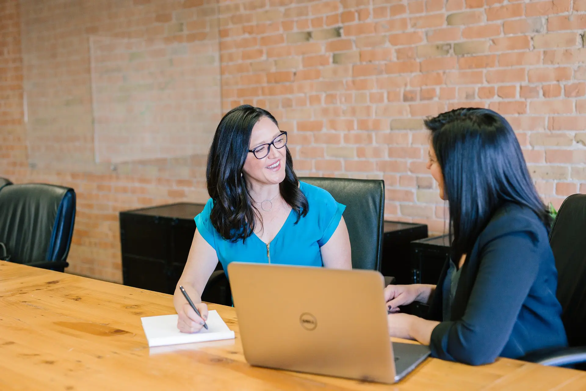 Two women on the same side of a table, talking to each other