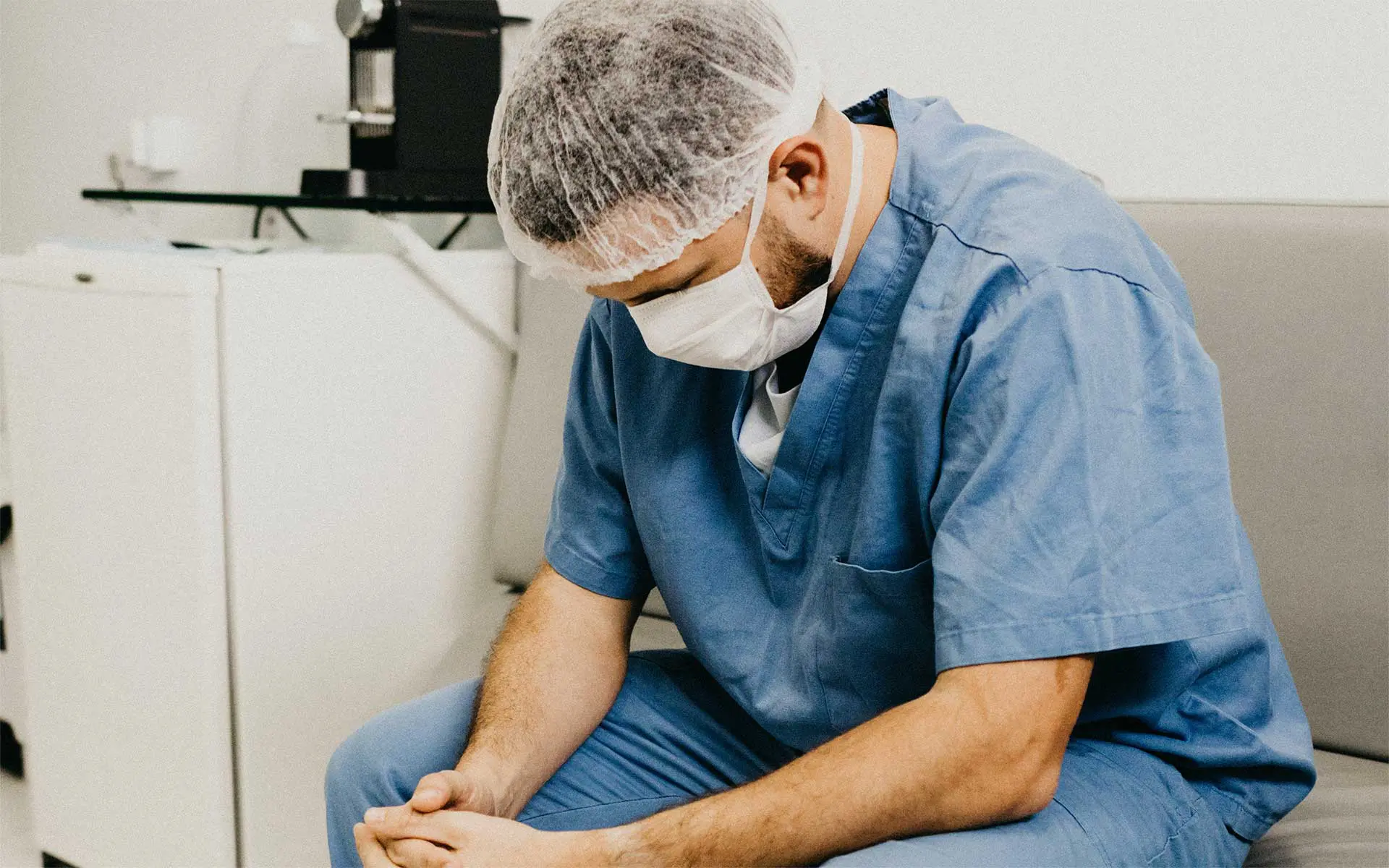 A man in nurse scrubs, wearing ppe, sat down, looking down at his hands