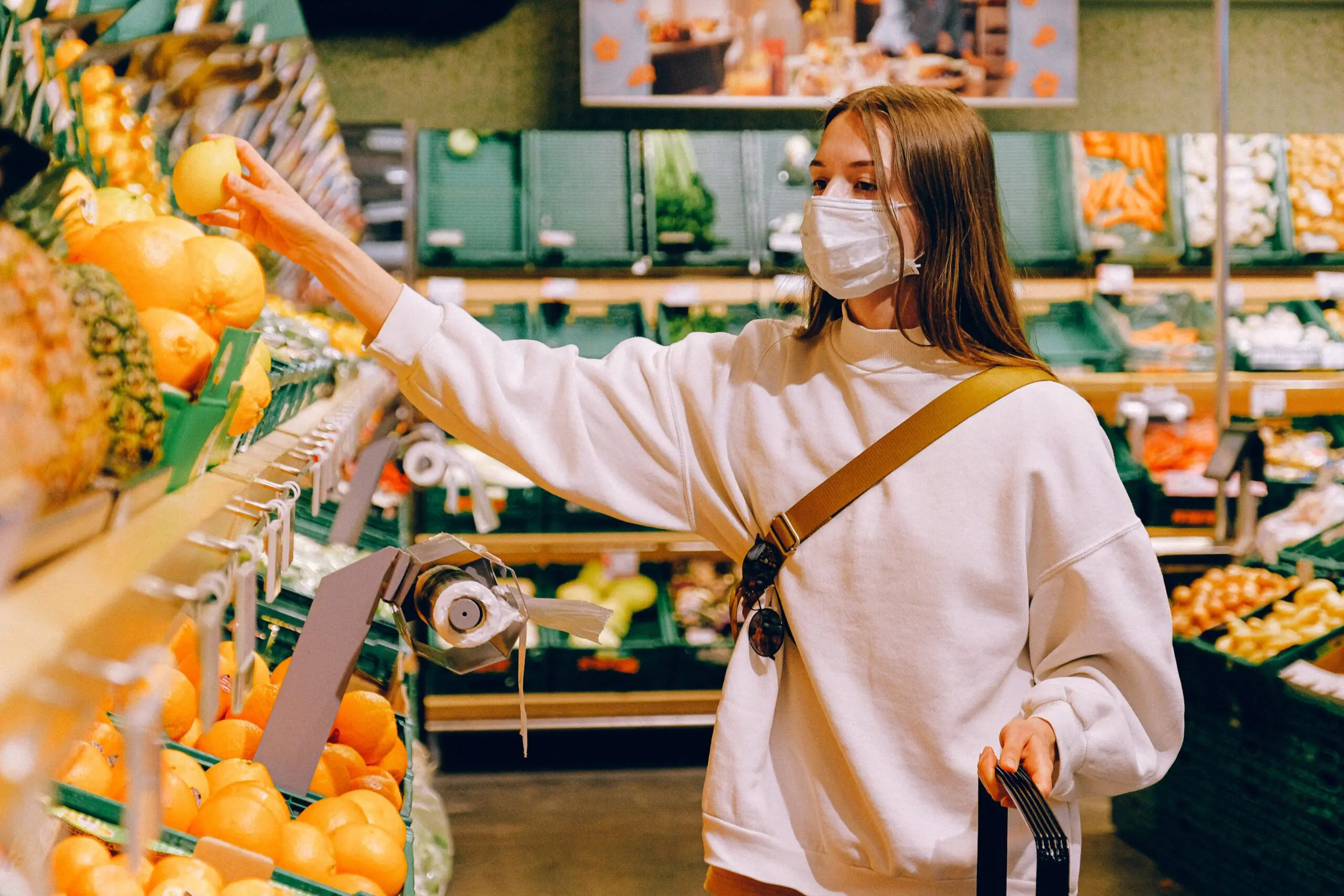 A woman in a mask picks a lemon from the fruit isle in a supermarket