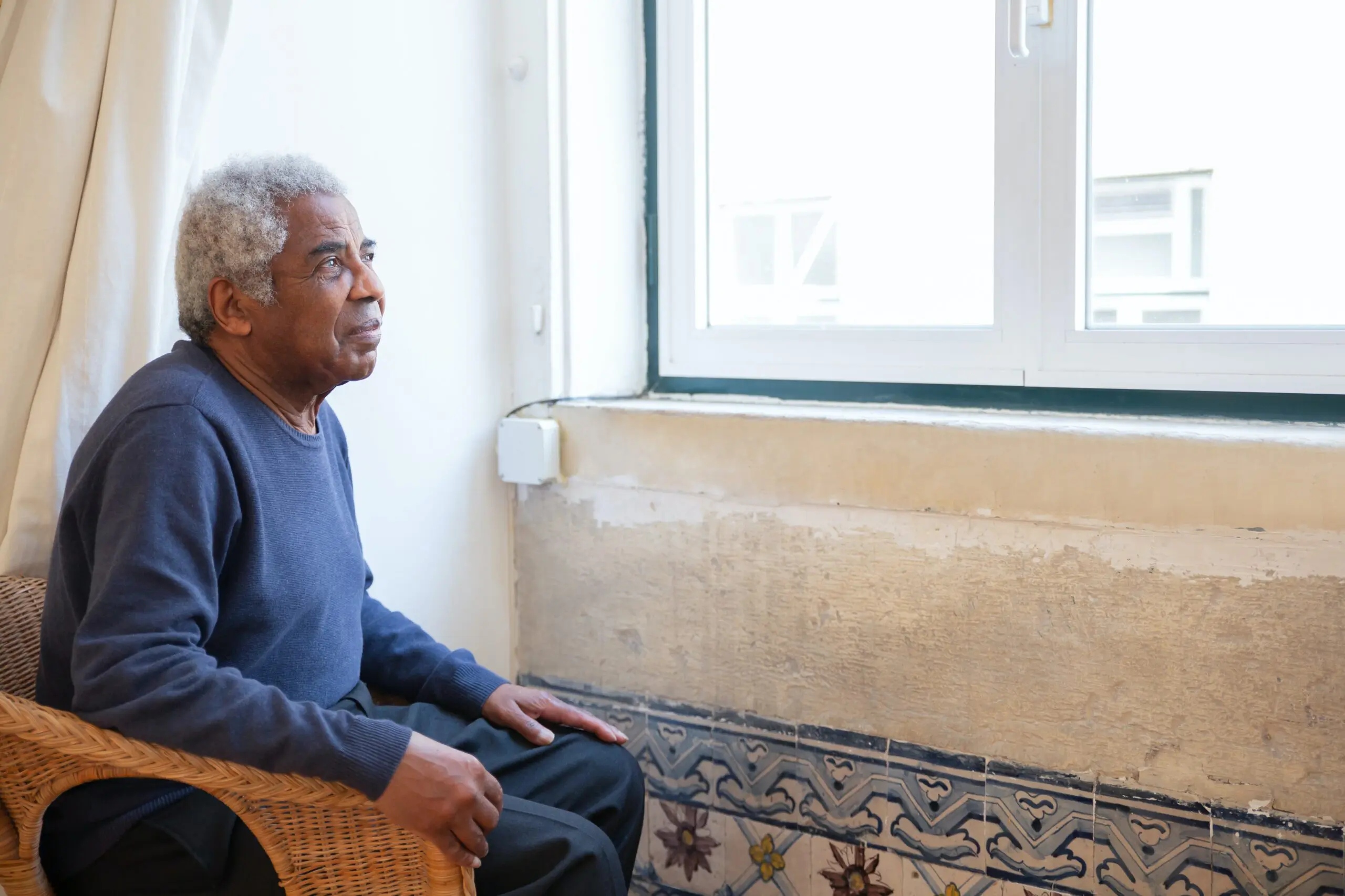 A person sat in a wicker chair looking out of a window