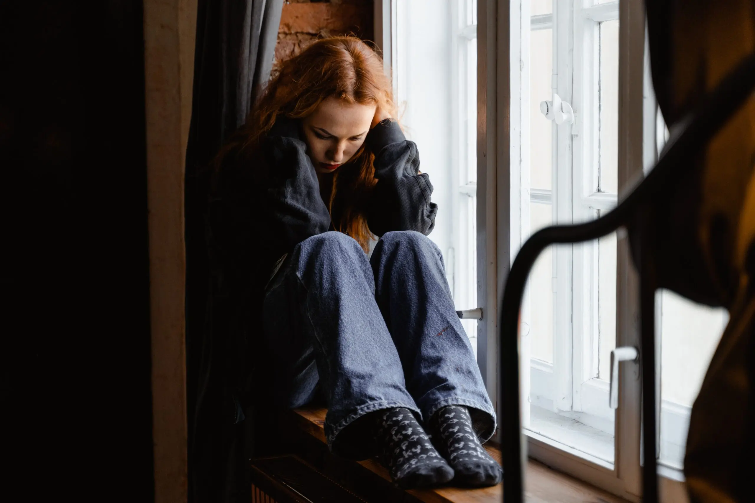 Someone sat on a windowsill with their head in their hands