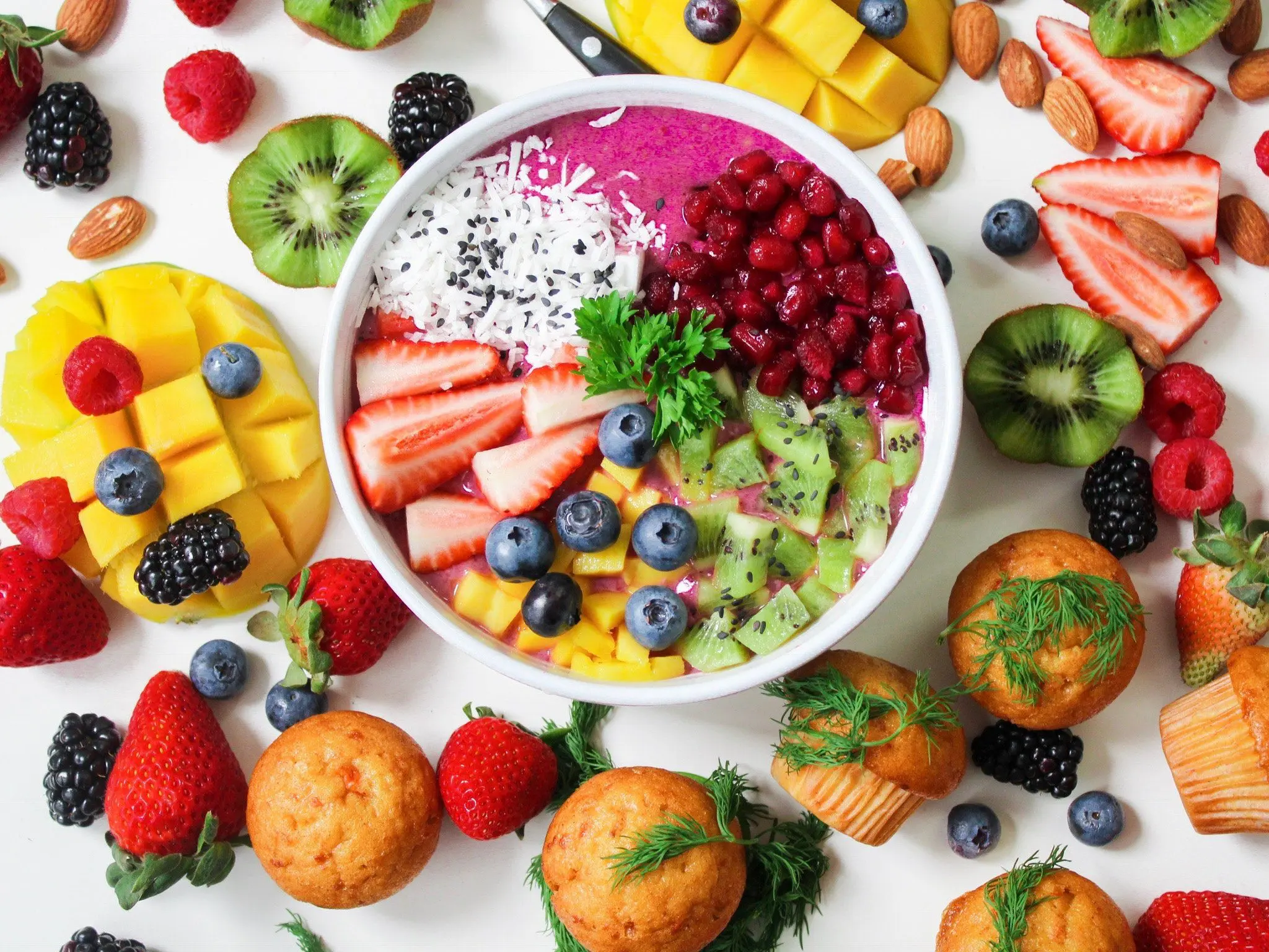 A large amount of food, mostly fruit, with a few muffins