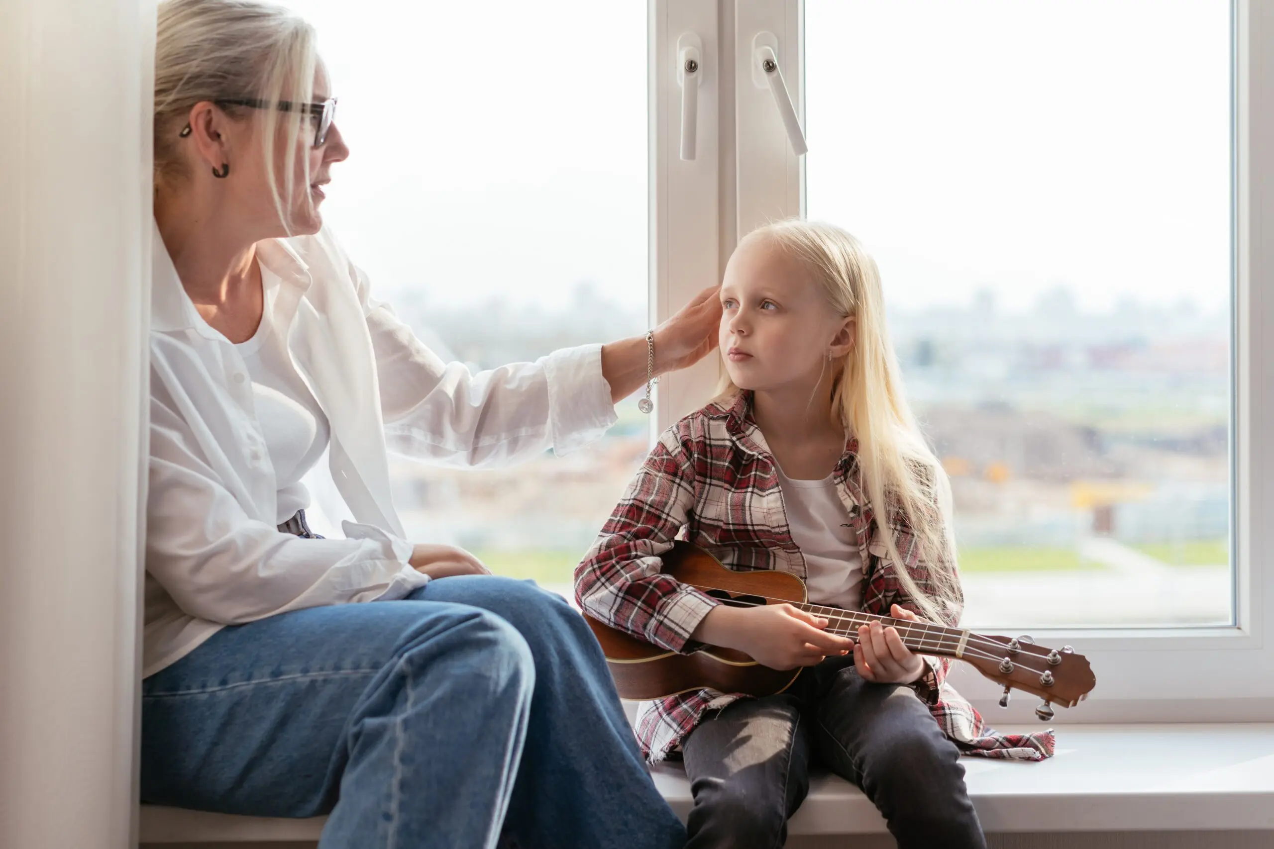 A woman brushing the hair out of the face of a child holding a ukelele