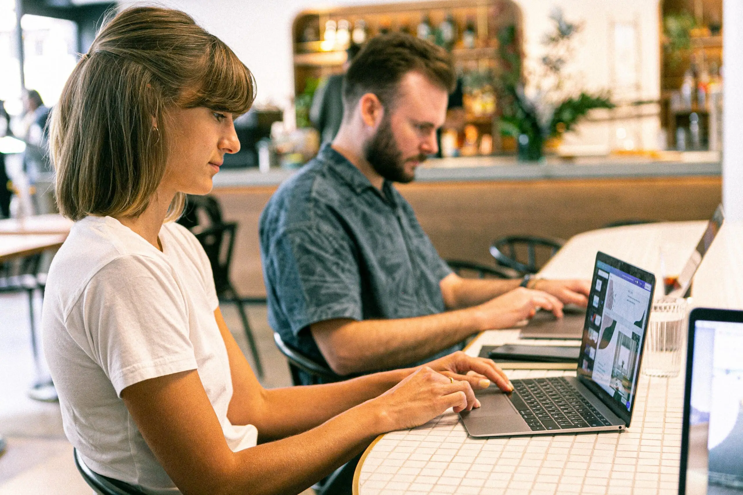 Two people in a cafe typing on laptops