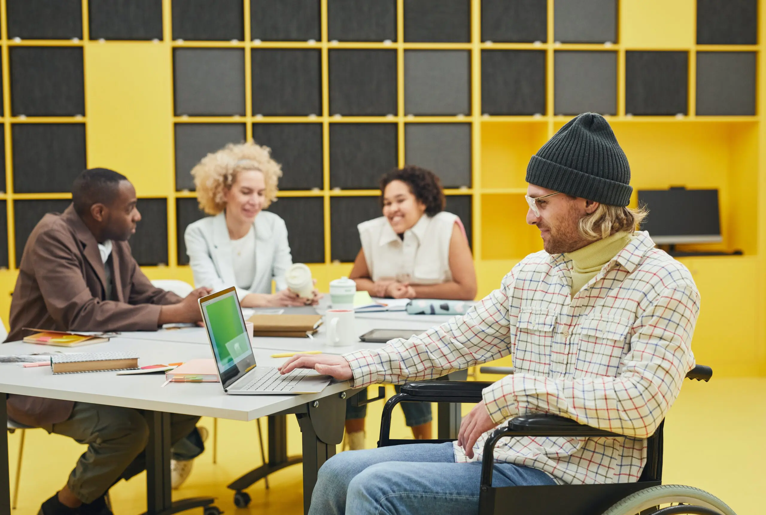 Man uses laptop while three people talk in the background