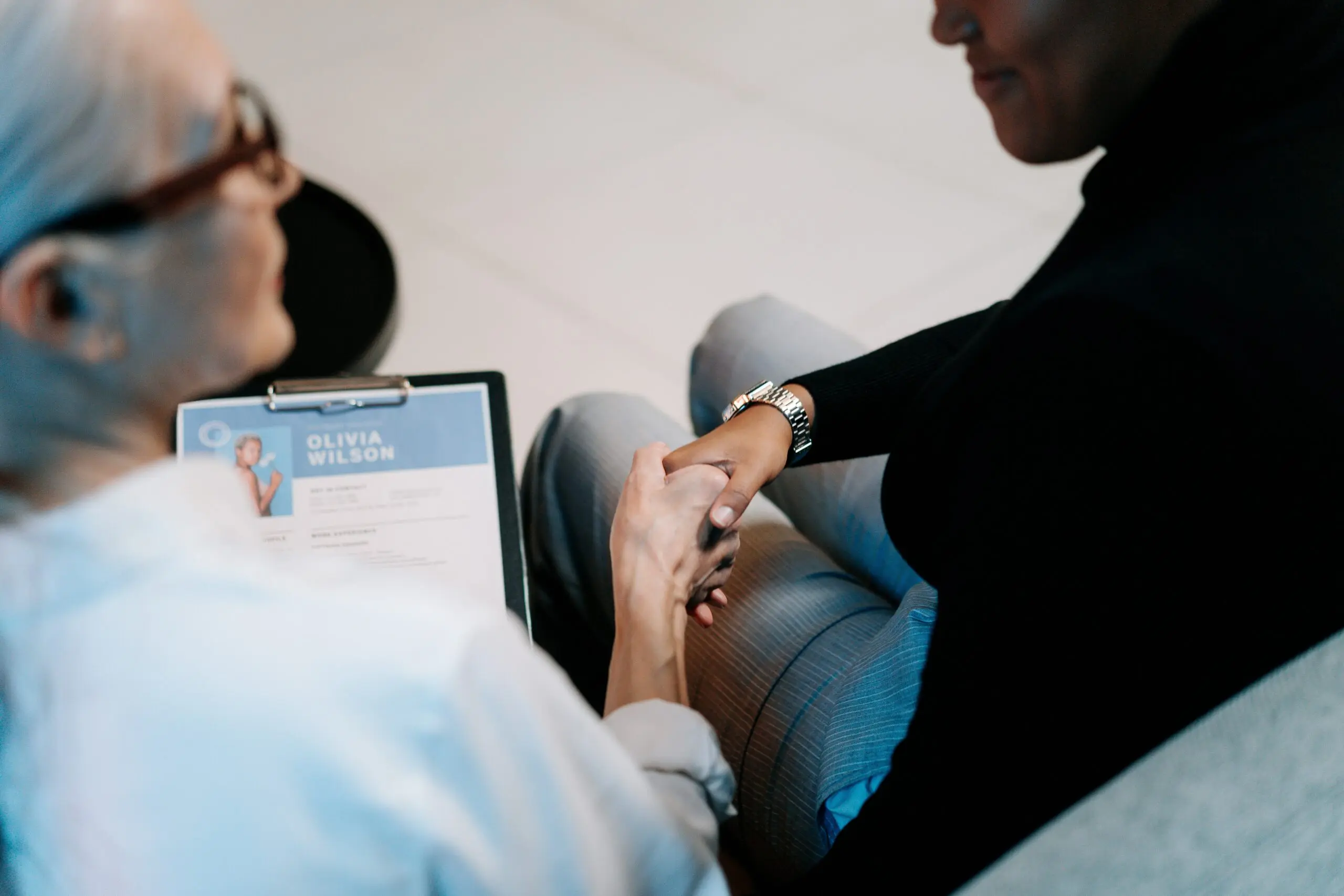 Two people holding hands on a sofa, one is also holding a clipboard