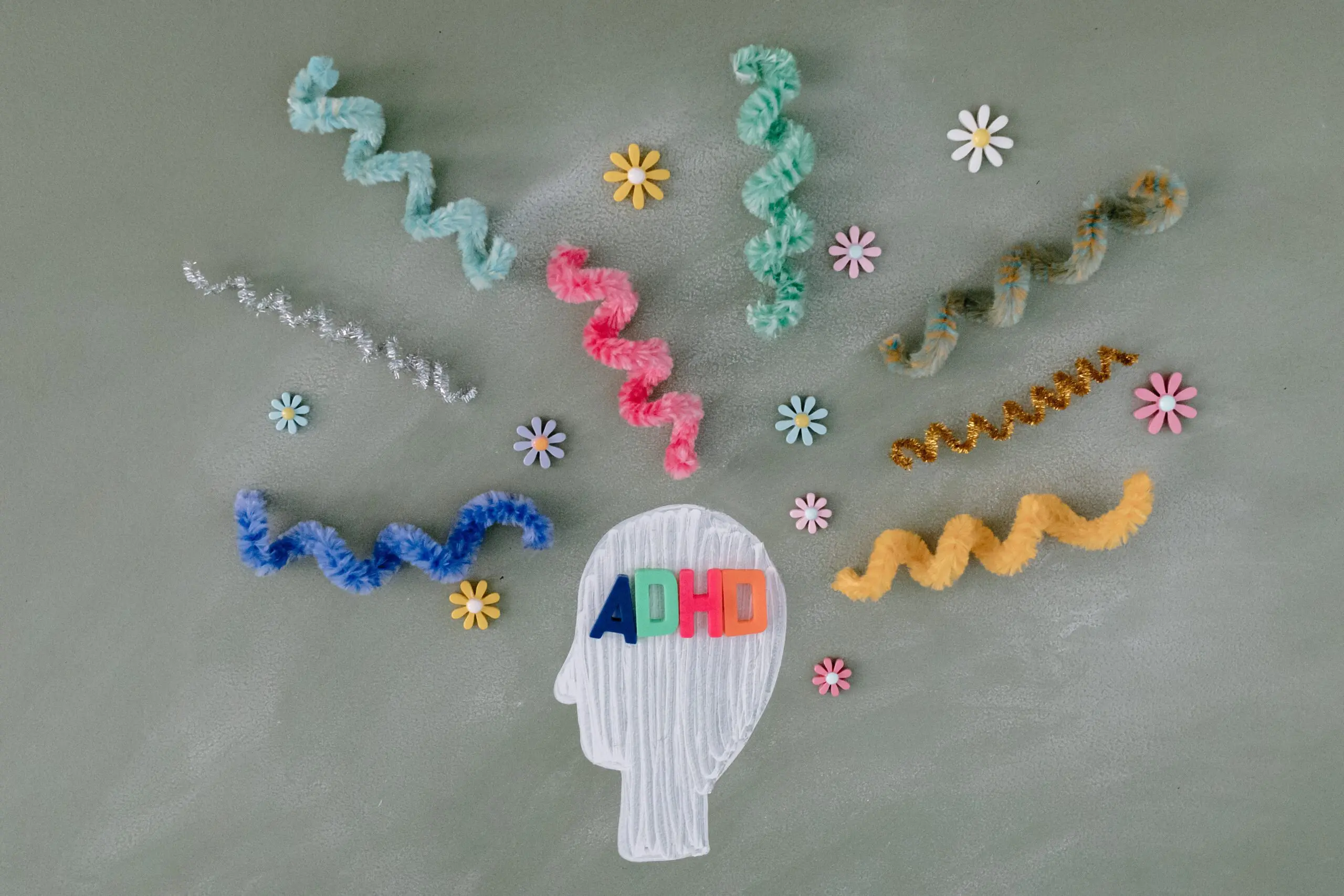 A wooden head with ADHD on it, surrounded by bits of furry string and flowers