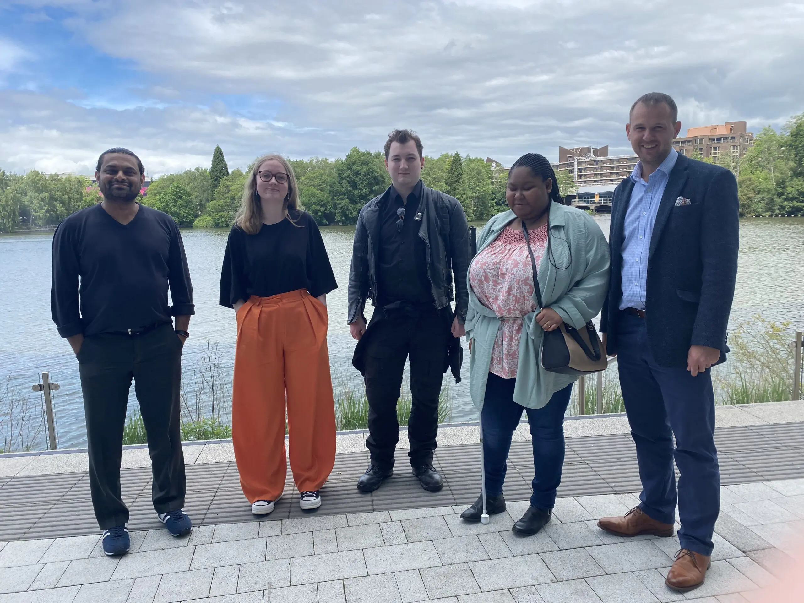 Five people stood next to each other by a waterfront smiling a the camera