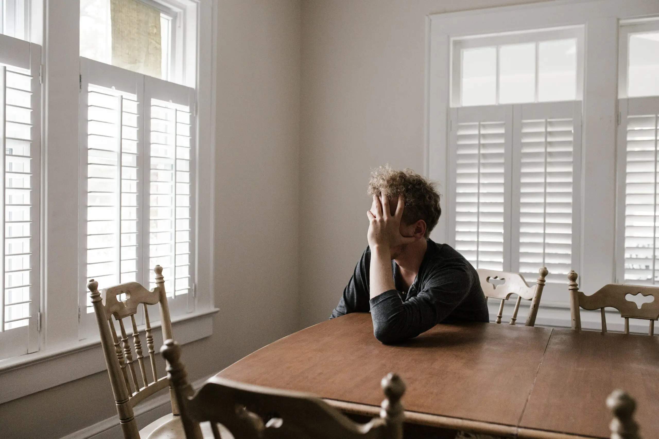 Someone with their head in their hand sat at a table, staring out of a window