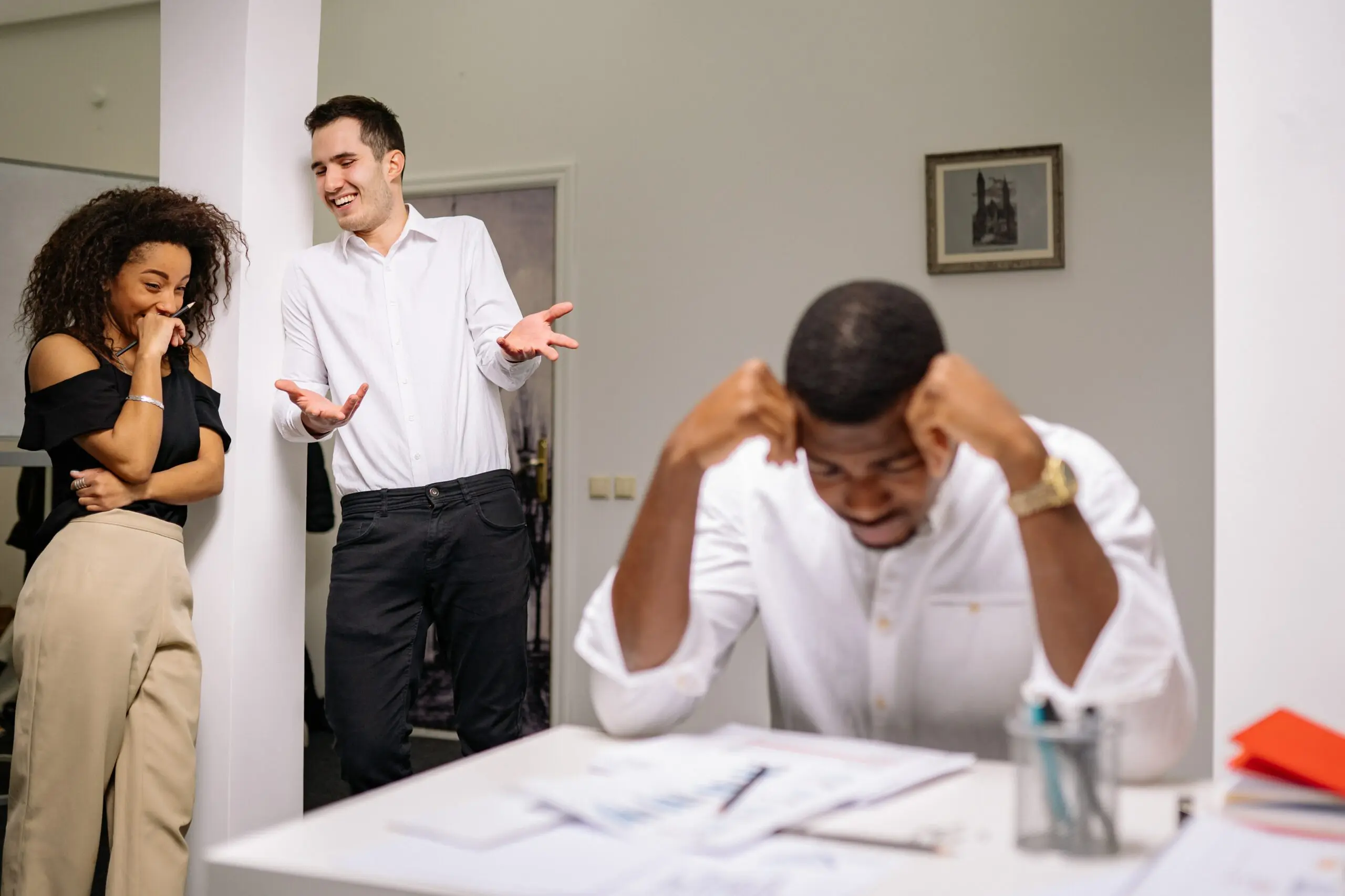 A man sat with his head in his hands, as two people laugh at him