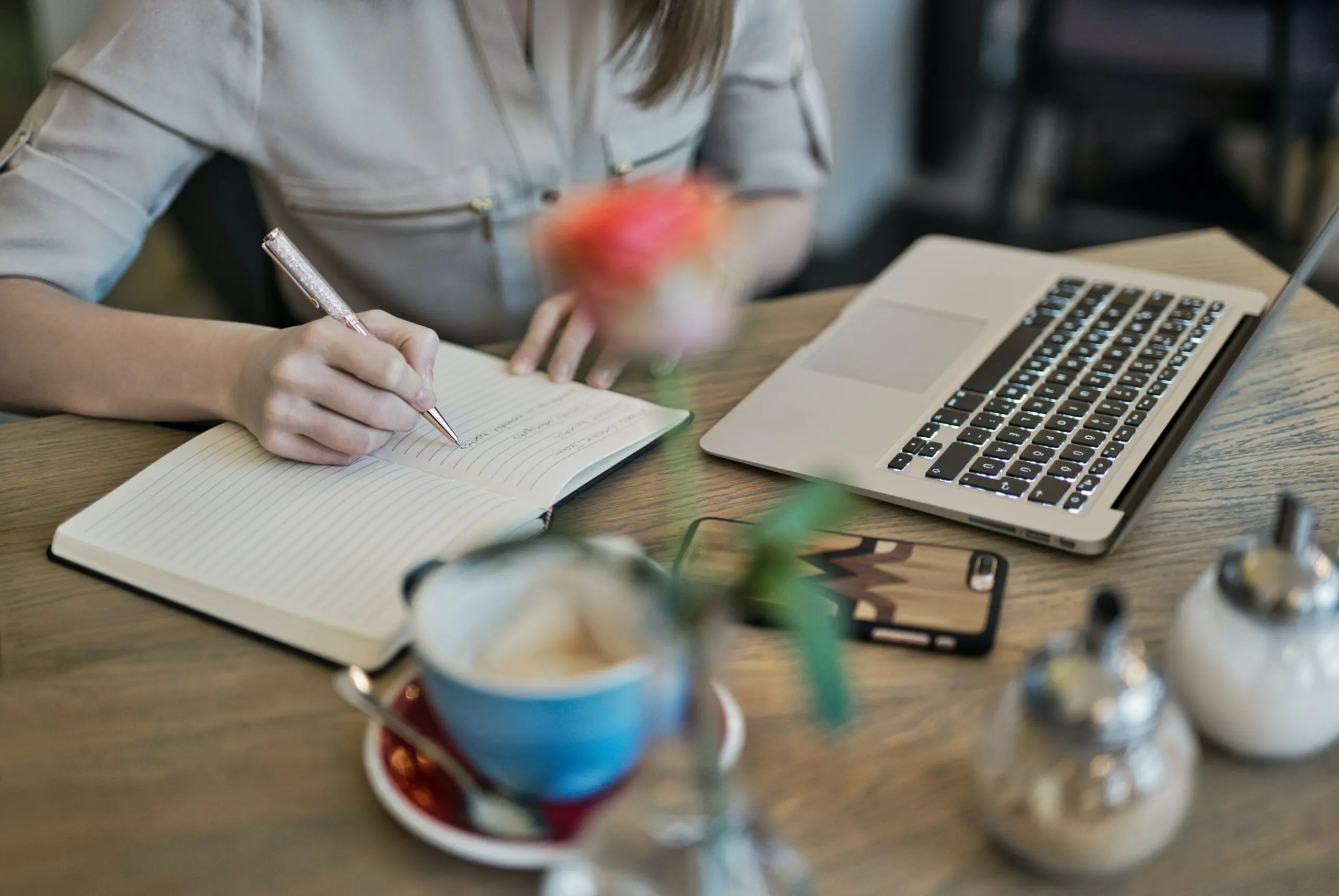 Someone writing in a notebook next to a laptop