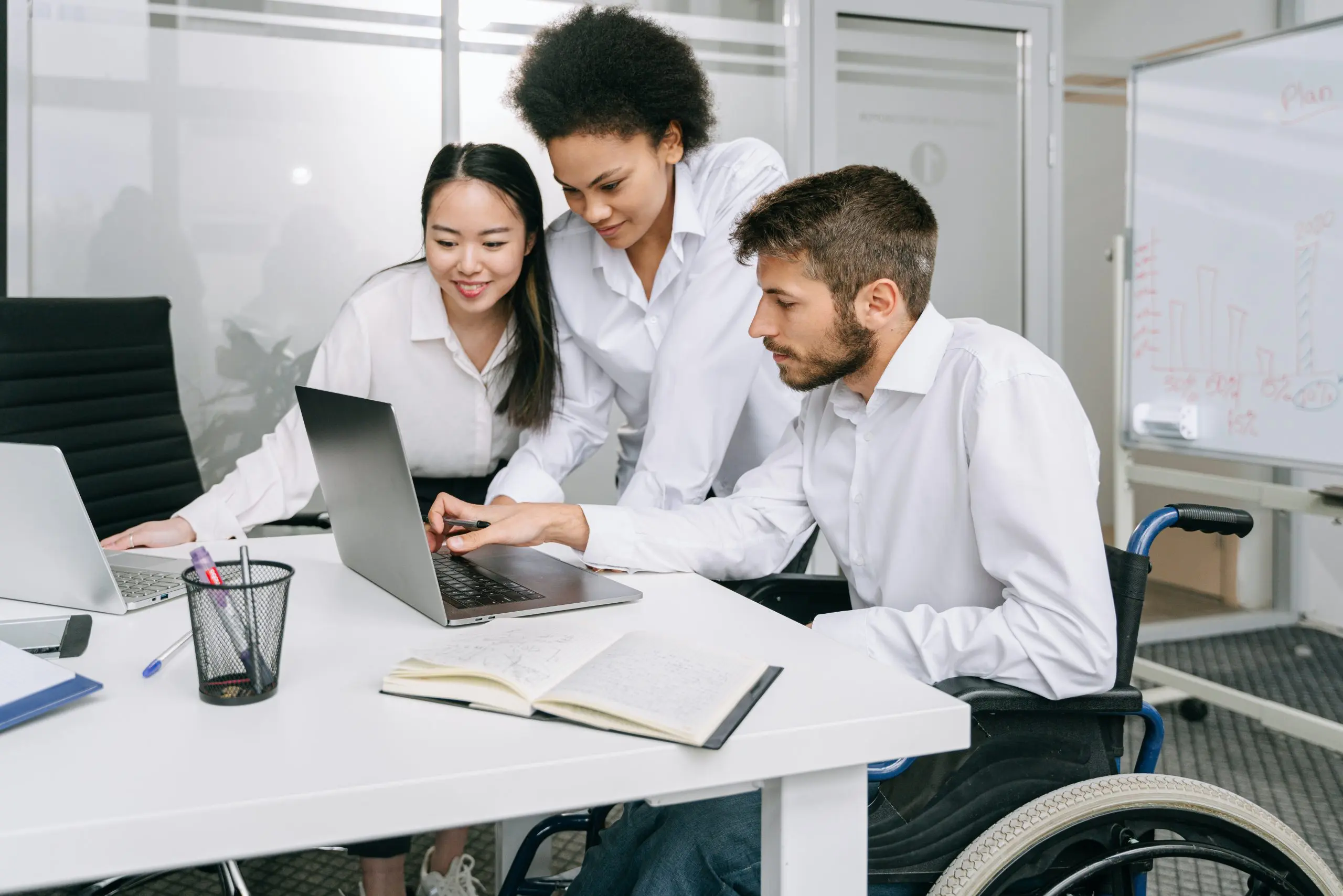 Three people around a laptop. One is in a wheelchair