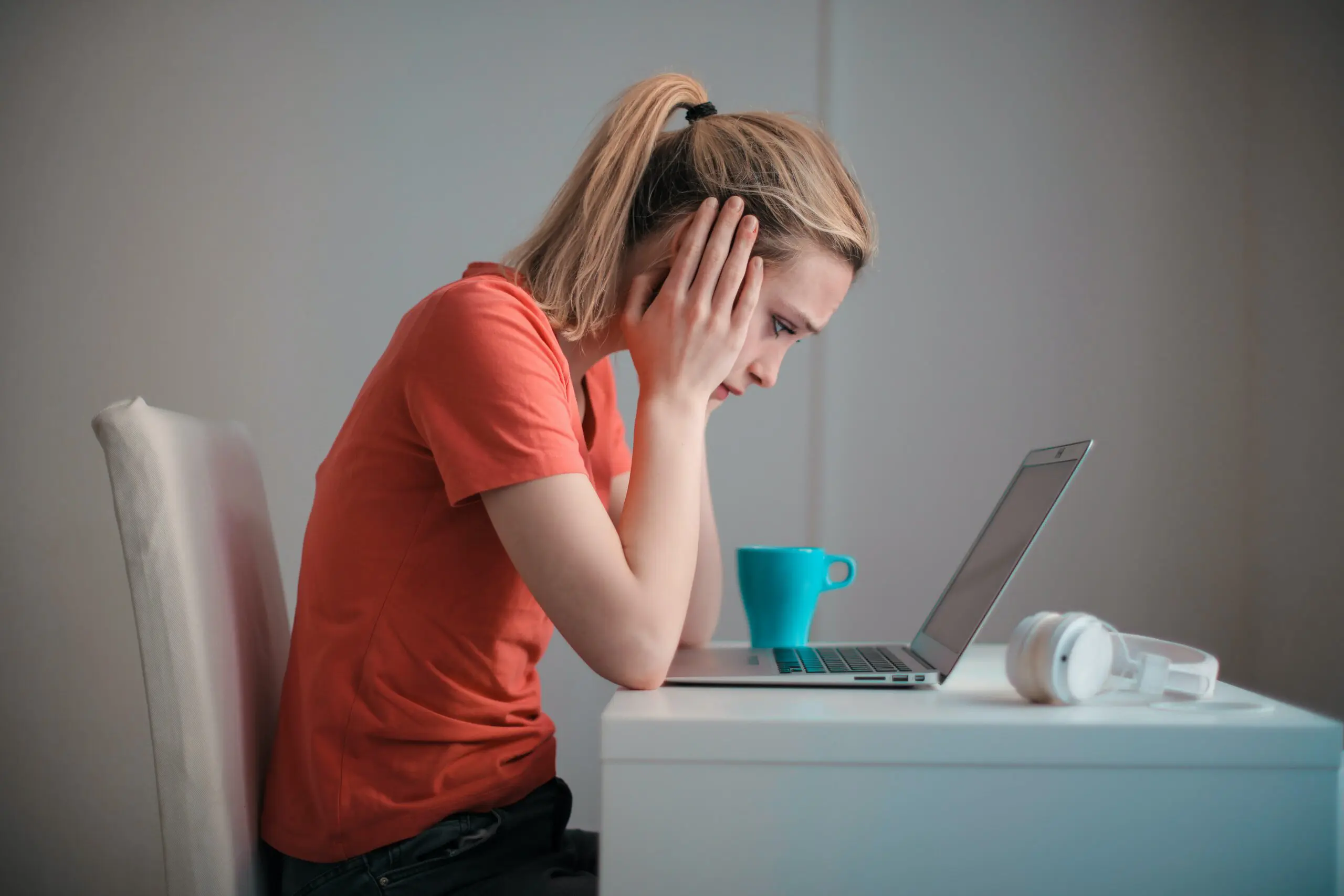 A woman with her head in her hands looking down at a laptop
