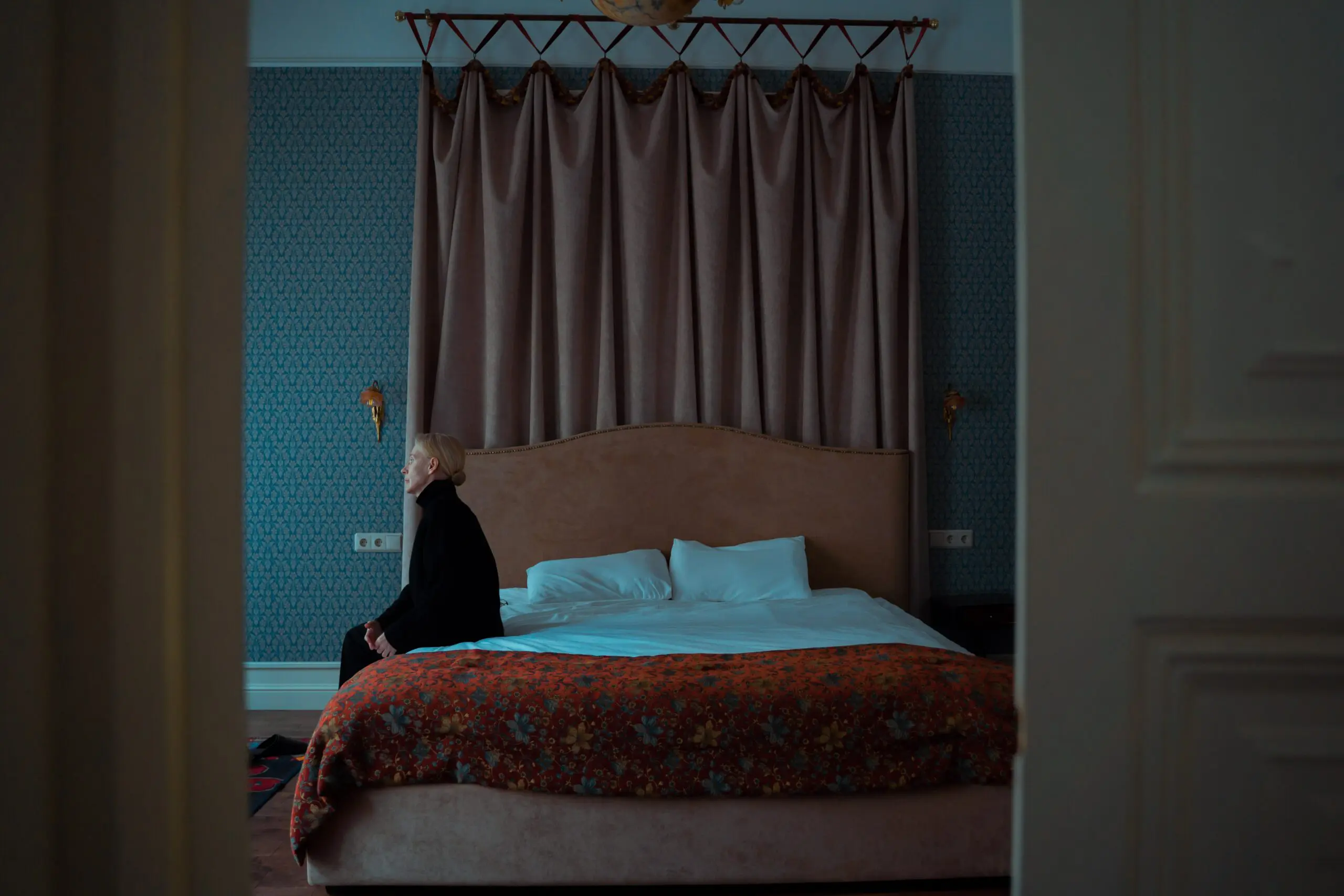 A woman sitting on the side of a large bed, staring off into the distance