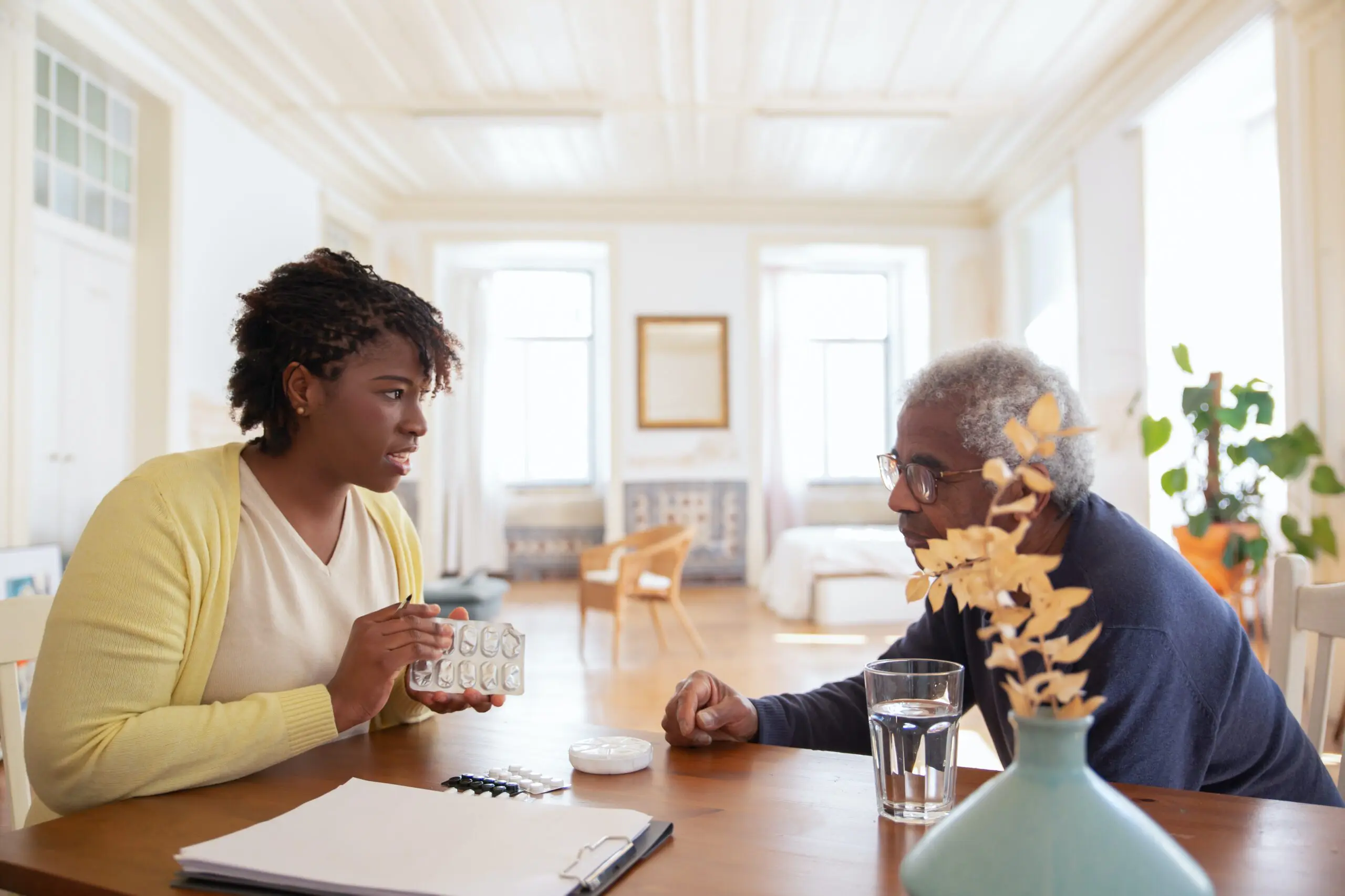 Two people talking over a table, one is holding a blister pack of medication