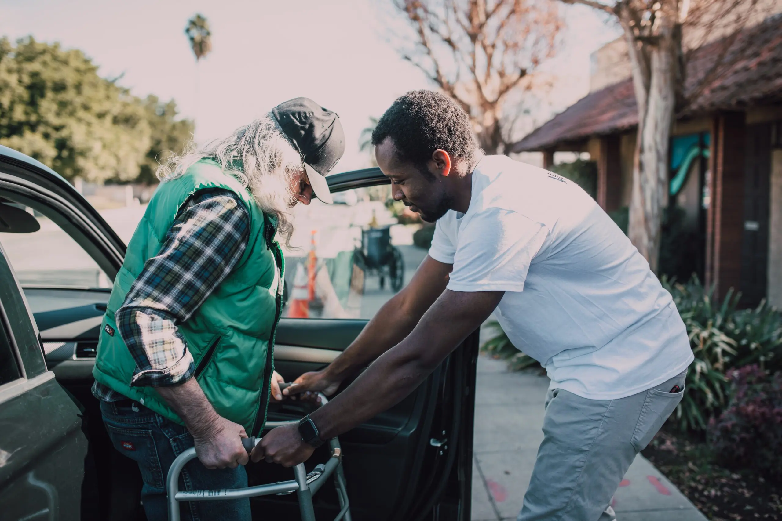 Man helping an older man out of a car using a walker