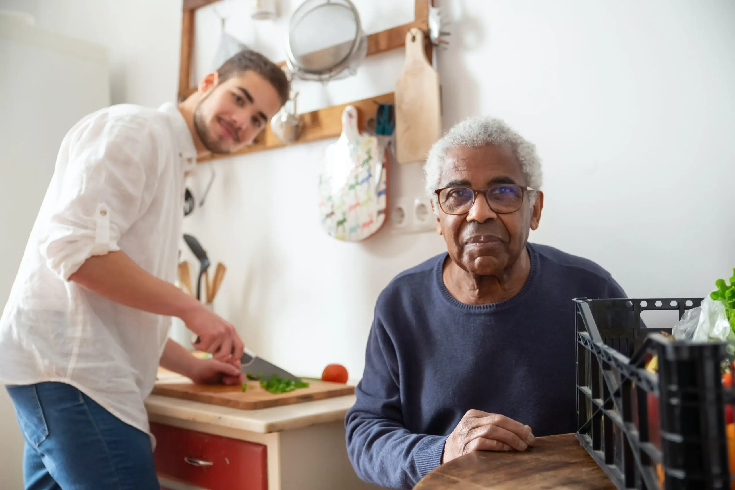 Someone chopping vegtables in the background, while an older gentleman in the foreground looks at the camera