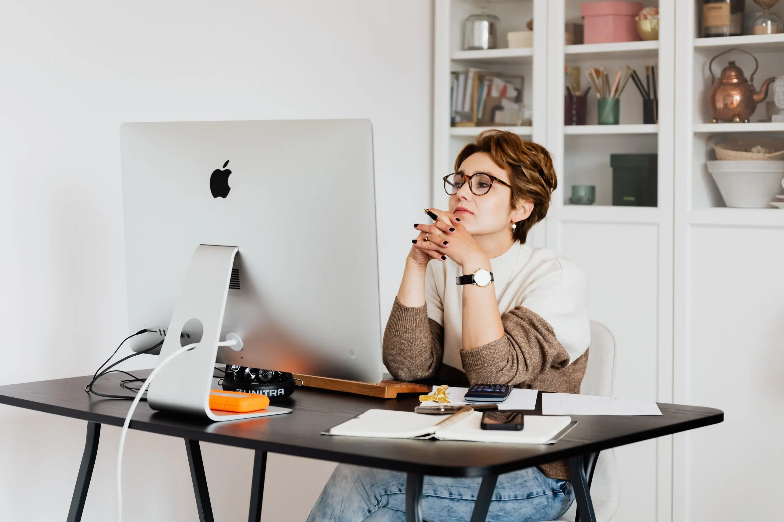 A woman, with her hands interlaced, looking at a computer