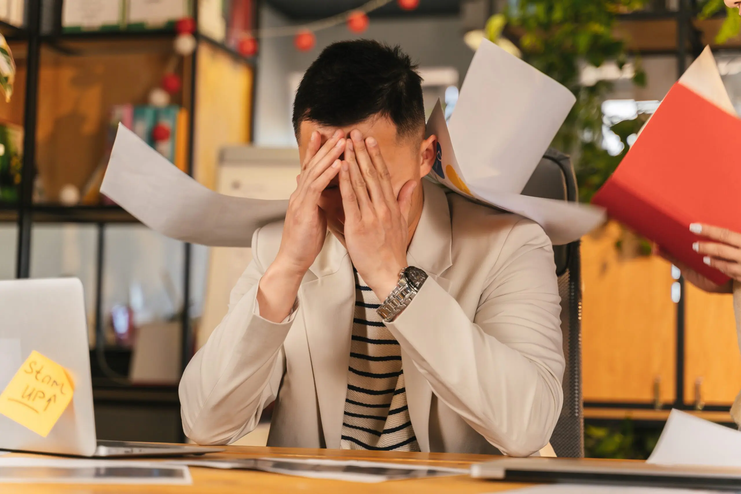 A man with his head in his hands being assaulted by flying paper.
