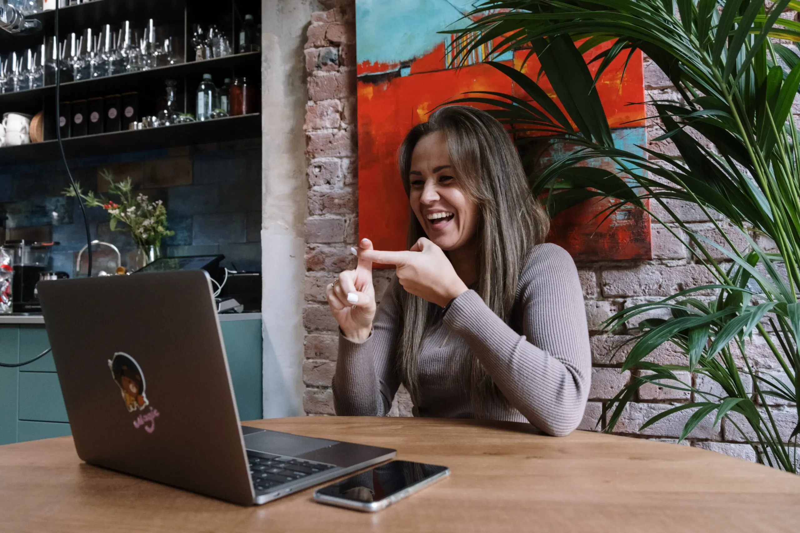 A smiling woman signing something with her hands in front of a laptop