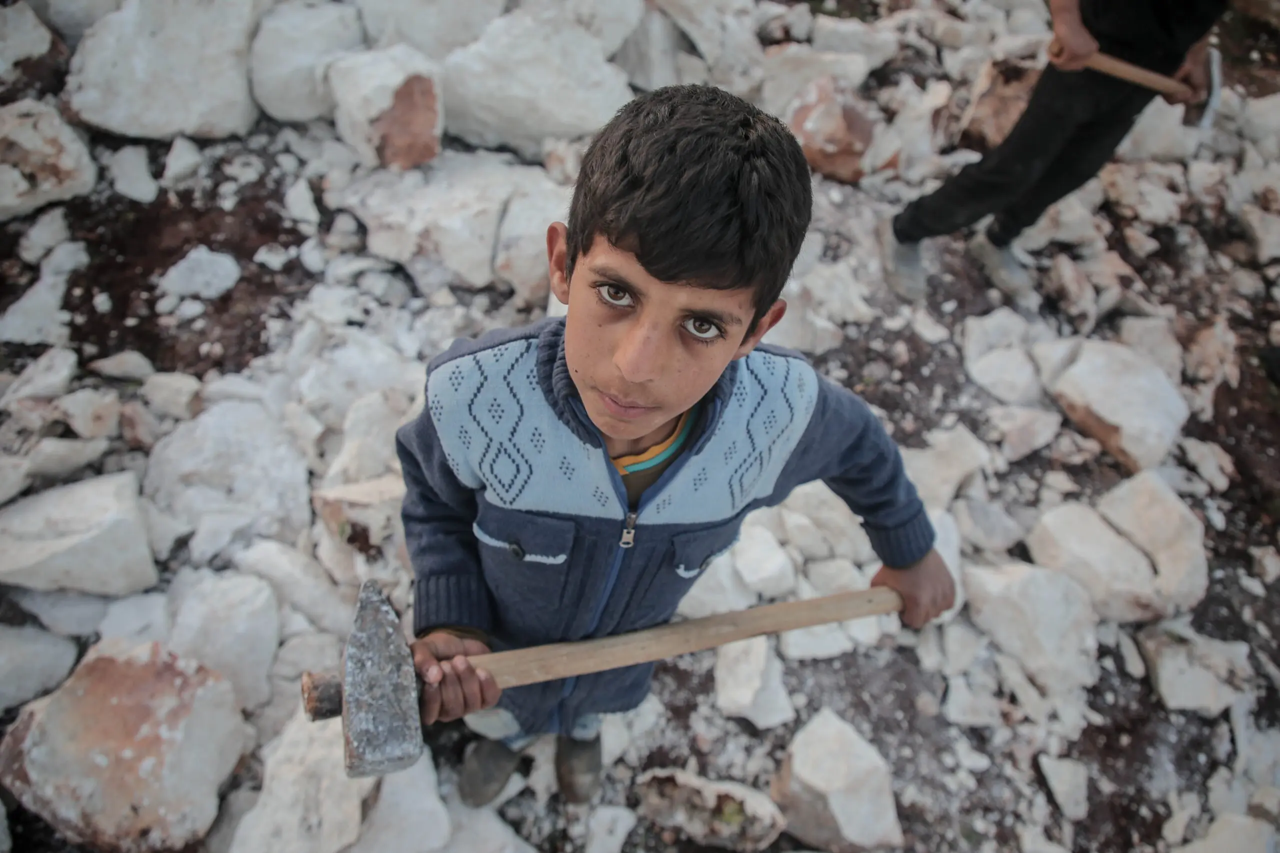 A young child holding a sledgehammer working in hard conditions