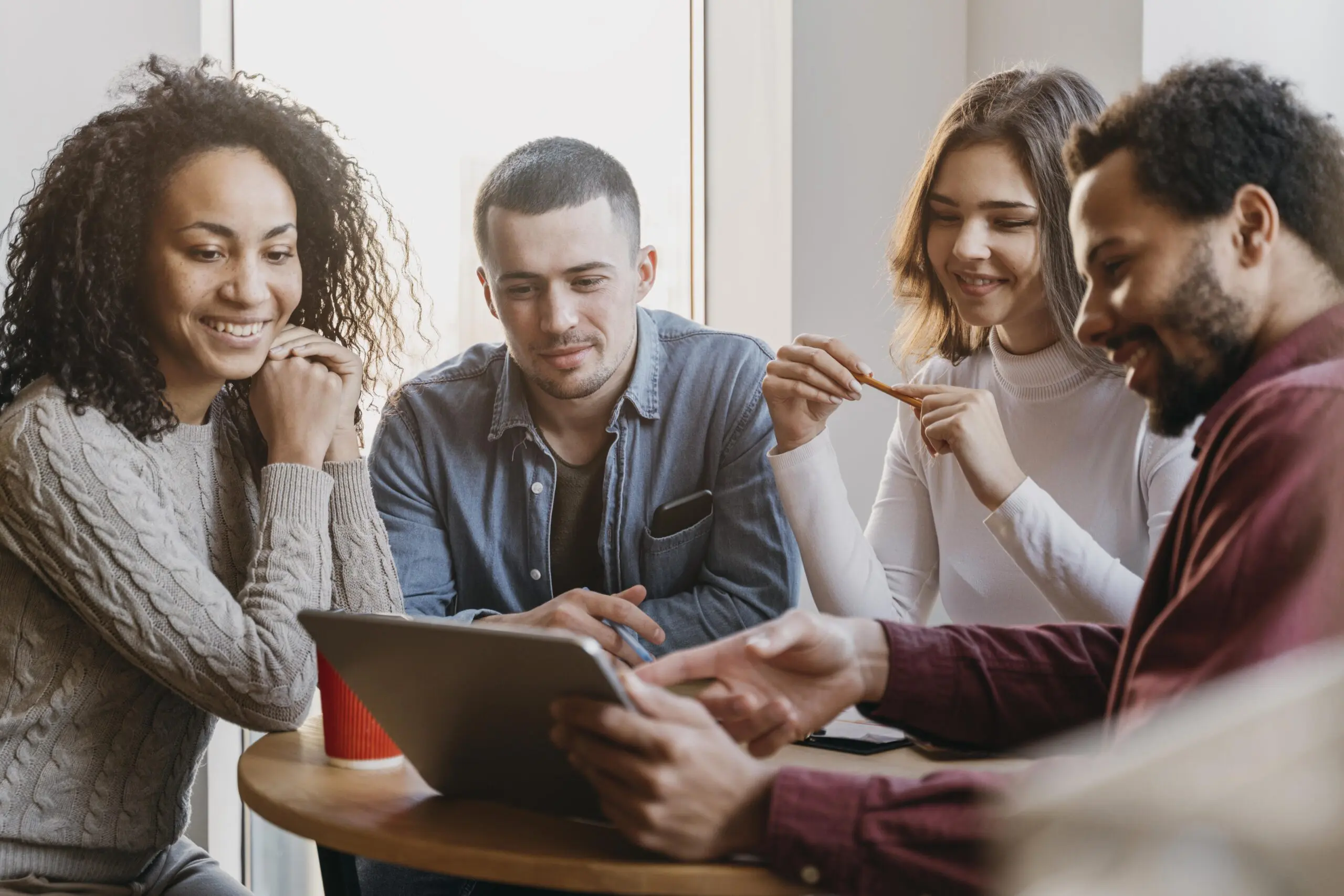 Four people gathered around a laptop looking at it and smiling