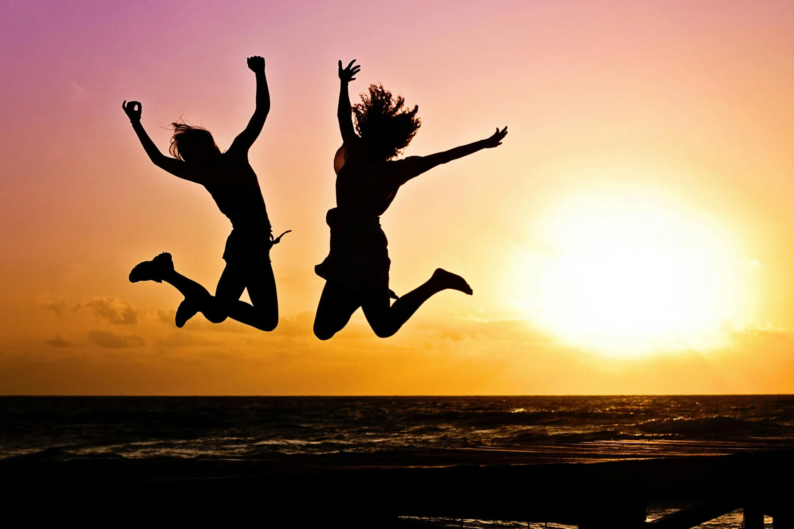 two-people-jumping-in-the-air-in-celebration-in-front-of-a-sunset