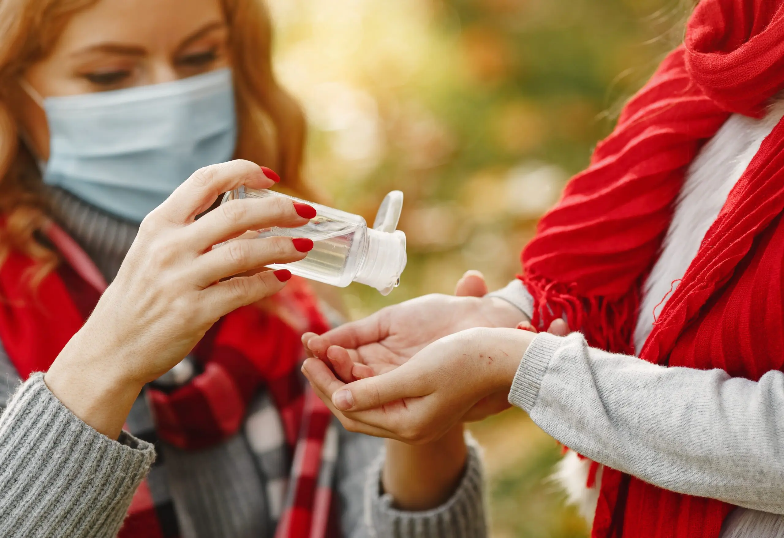 woman-giving-hand-sanitizer-to-her-friend-while-wearing-a-face-mask-scarf-hat-and-other-warm-clothing
