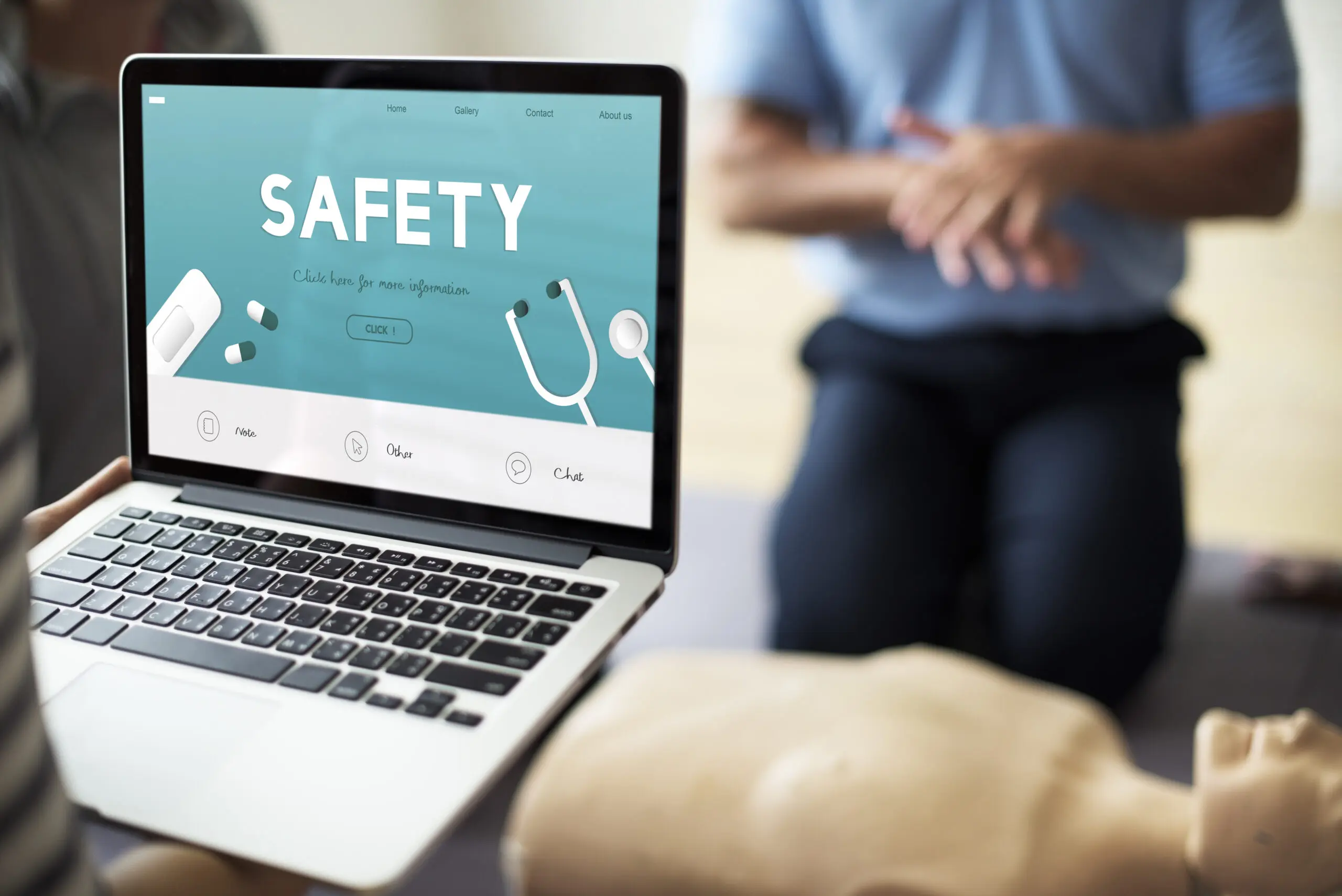 laptop showing the word SAFETY in bold and in the background their is something administrating CPR in a training session