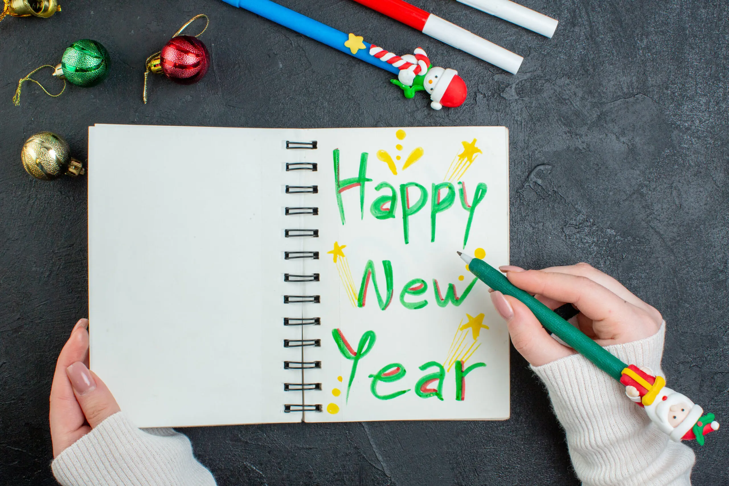 top-view-hand-holding-pen-spiral-notebook-with-happy-new-year-writing-decoration-accessories-black-table