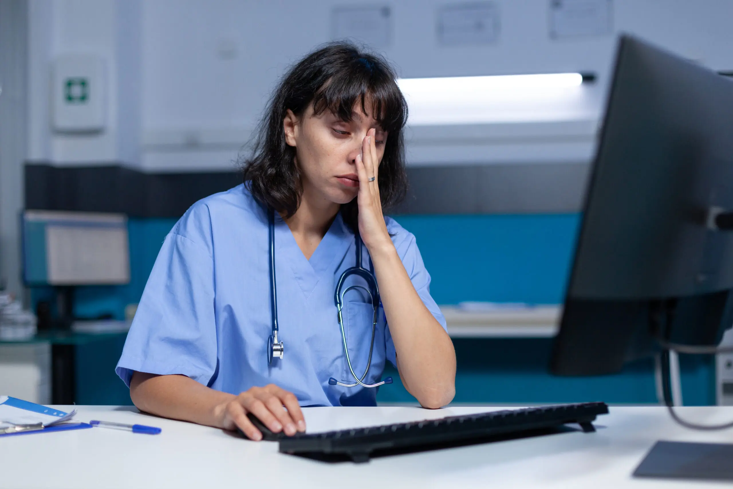 Medical assistant falling asleep while using computer and keyboard due to working late as she is being overworked