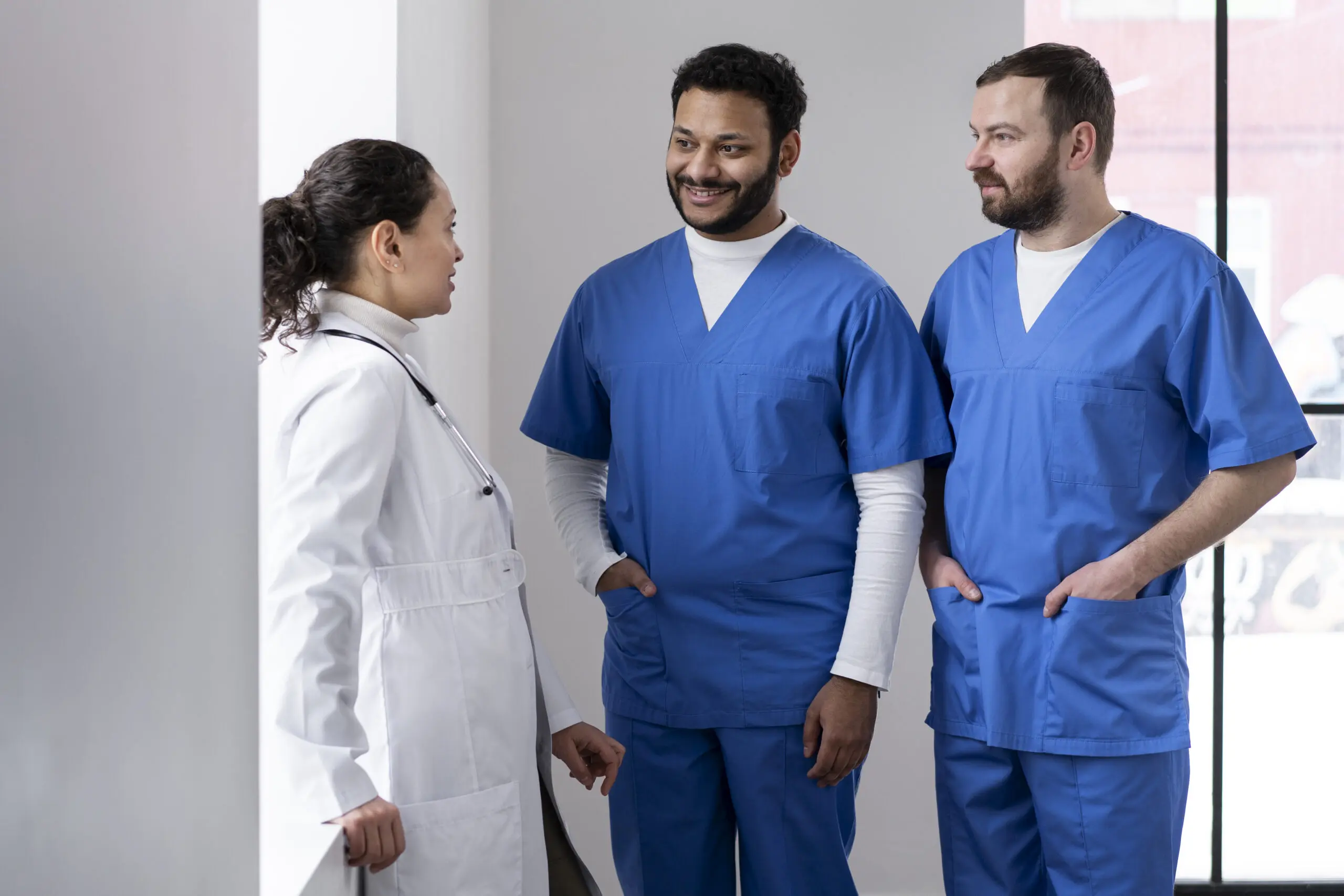 care staff team members encouraging each other to progress in their work. Two men in blue scrubs and one woman in white