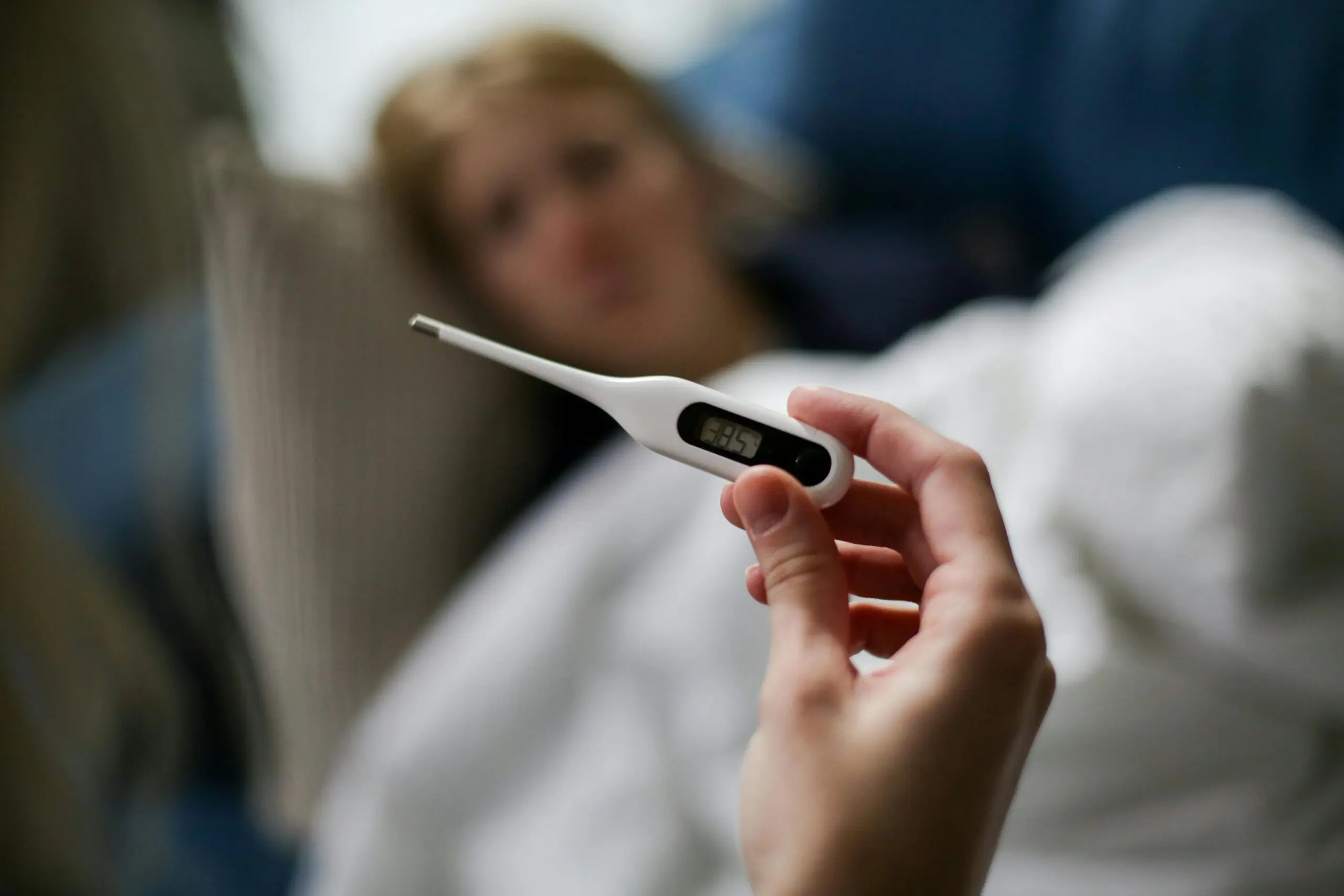 woman who is ill led on a sofa while another woman takes her temperature