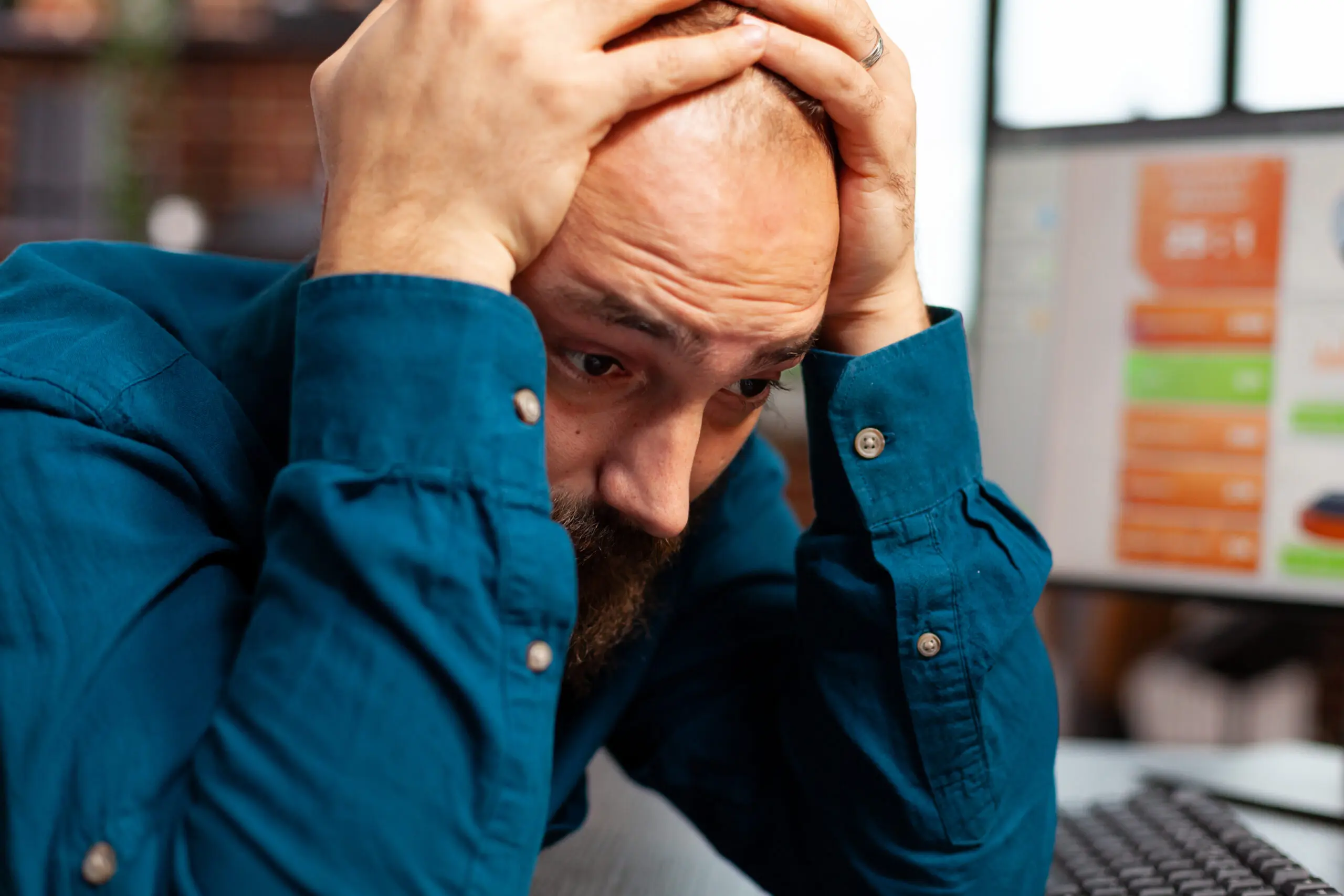 stressed man with hands on his head, hunched over his desk
