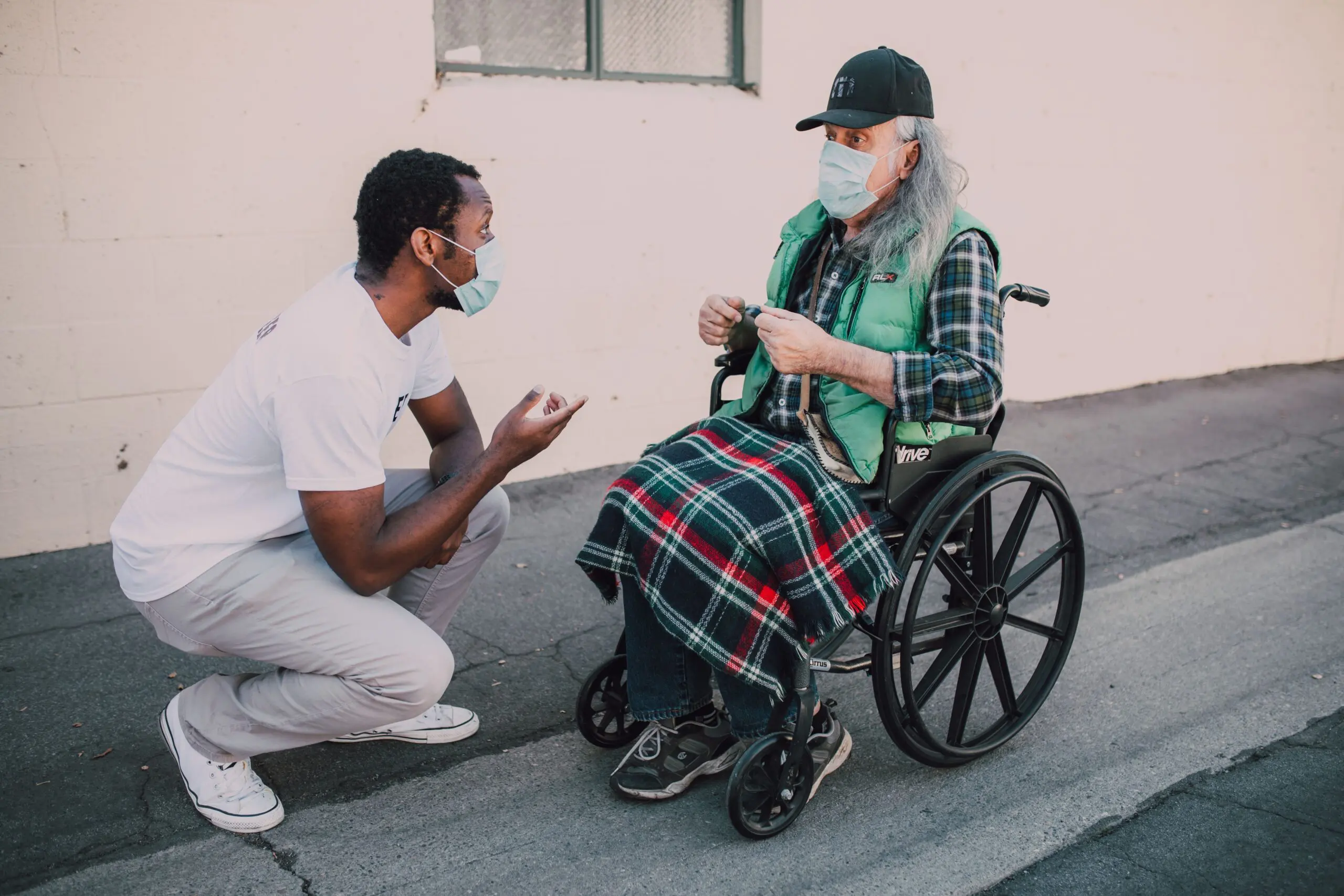 black male mental health support worker supporting elderly white man in wheelchair
