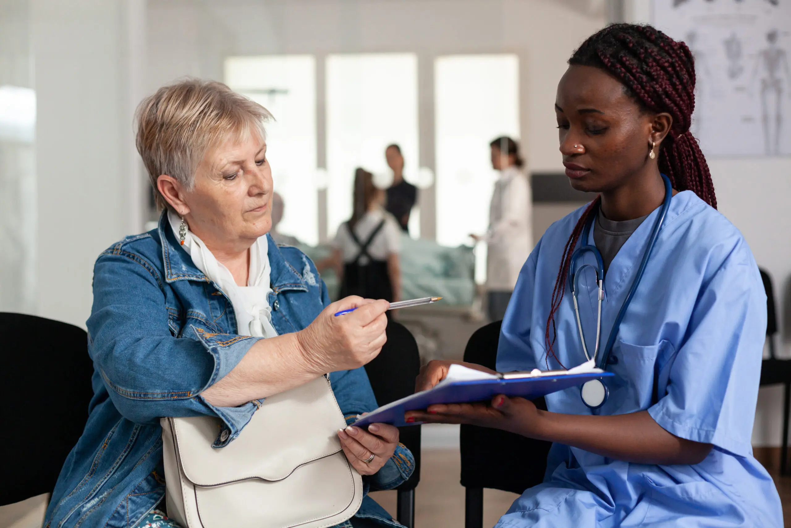 black female care worker helping female elderly white patient to sign documents