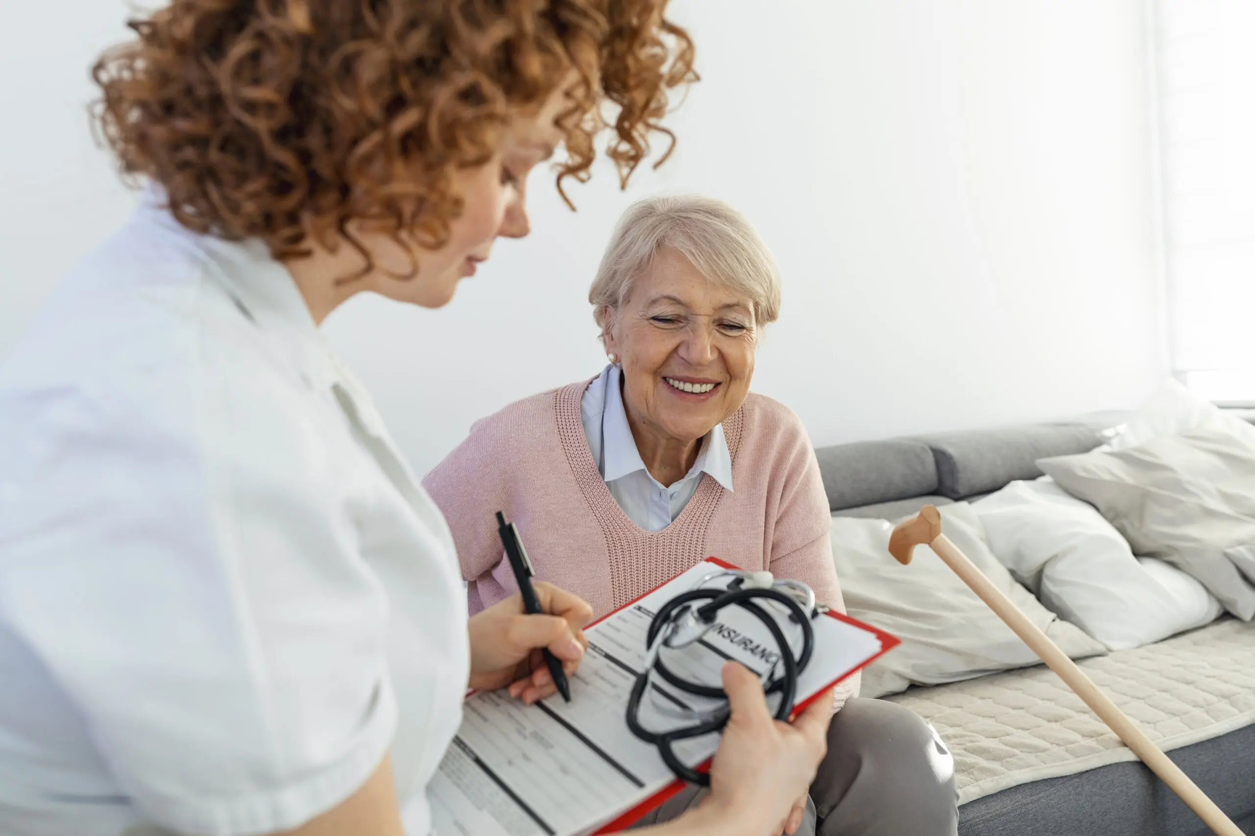 Senior woman is visited by her doctor or caregiver. Female doctor or nurse talking with senior patient. Medicine, age, health care and home care concept. Senior woman with her caregiver at home