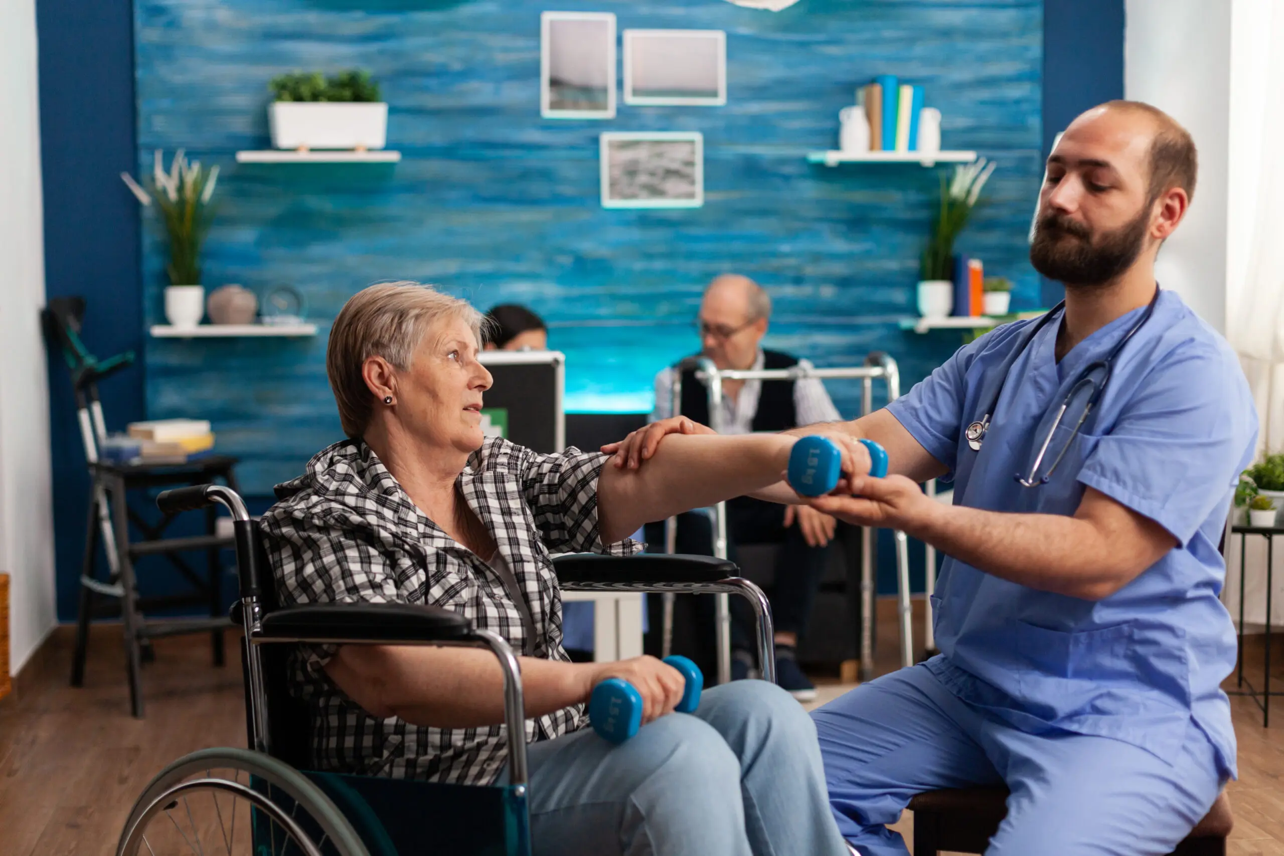 white male nurse and elderly female patient in a wheelchair using weights with assistance of the nurse