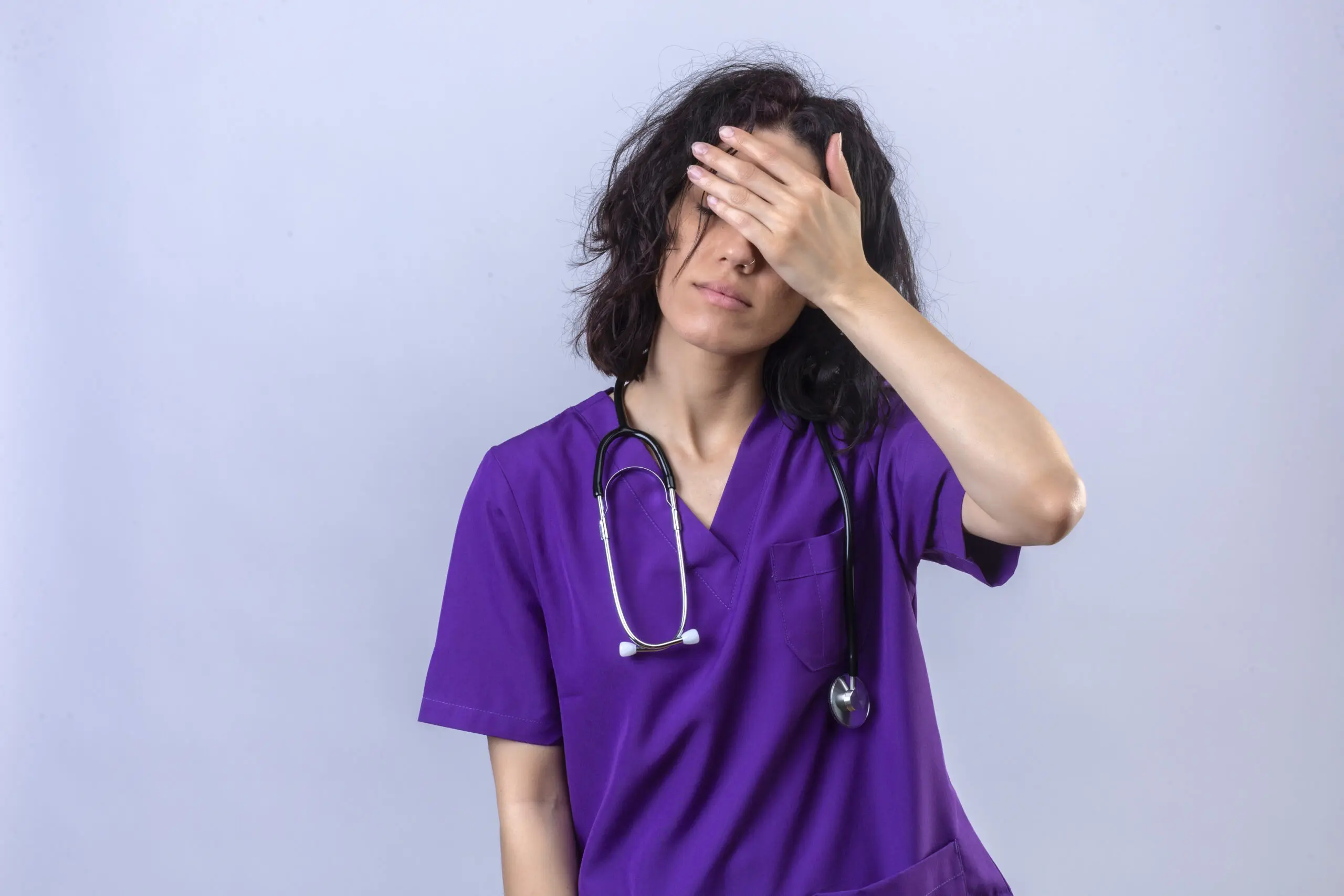 female nurse in purple scrubs with her hand on her head, showing stress