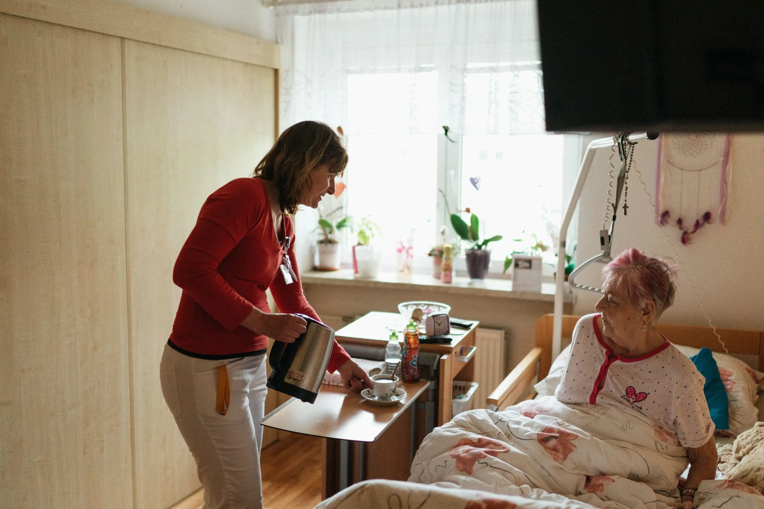 care worker pouring a cup of tea for elderly woman in bed at a care home