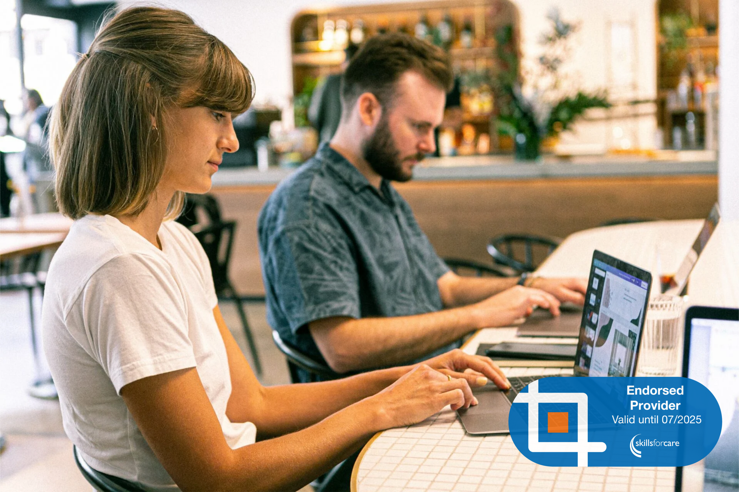 Two people in a cafe on their laptops. At the bottom right corner is the Skills For Care Endorsed Provider logo